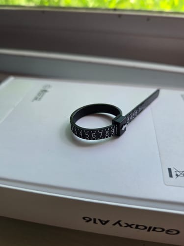 Customer's black FREE RING SIZER looped to show its numbered measurements while resting on a white box.
