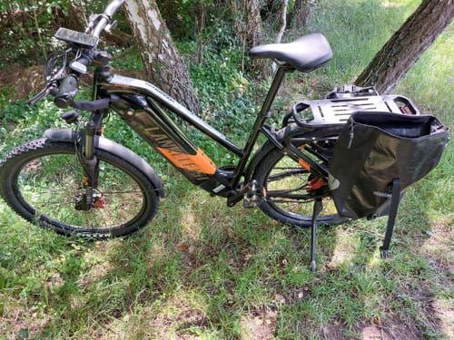 Customer's Lankeleisi MX600 Pro e-bike with a pannier bag on the rear rack, parked on a grassy path.