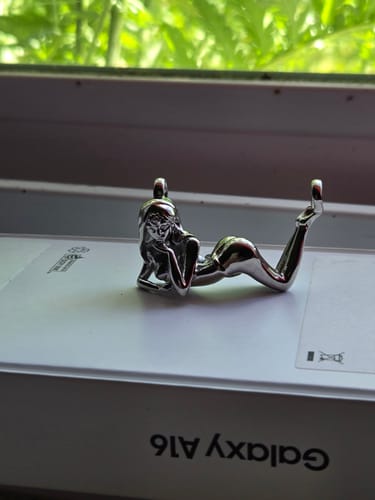 Reviewer's full body Succubus Pendant in shiny silver, resting on a white box by a window.