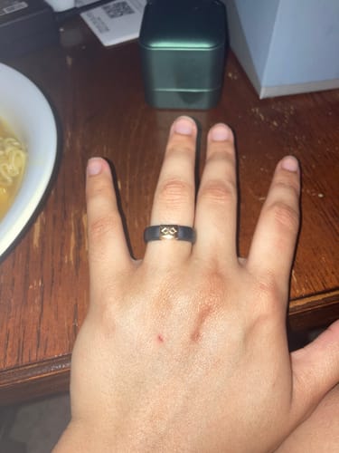 A customer's hand wearing the black silicone MetalInfinity ring with a gold-colored infinity symbol.