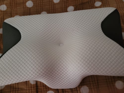 Vásárló fehér és szürke színű, ergonomikus anatómiai párnája egy ágyon.