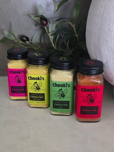 Reviewer's four shakers of Chooki's Chicken Salt, with varied colorful labels, lined up on a counter.