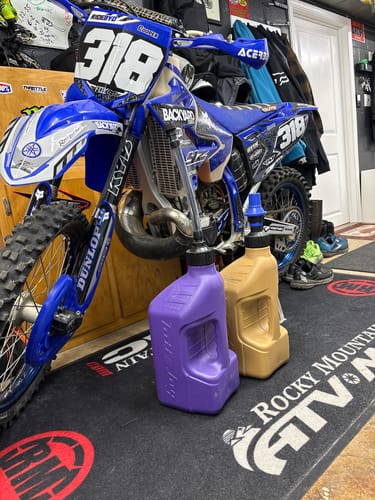 Customer's two fuel jugs sitting on a mat in front of a blue dirt bike.