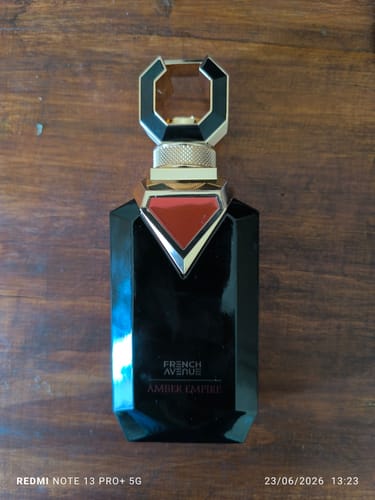 Reseñador muestra el perfume French Avenue Amber Empire en su elegante frasco negro sobre una superficie de madera.