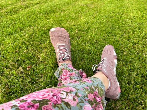Customer's feet propped up on green grass, wearing comfortable pink Smart II Barefoot Shoes.