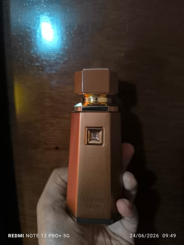 Una clienta sostiene en su mano el frasco de perfume Liquid Brun, de elegante diseño en color bronce.