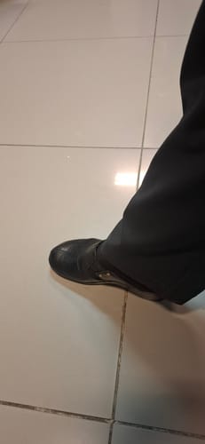 Customer wearing the black Taryn 1 Wedge shoe with black trousers on a white tiled floor.