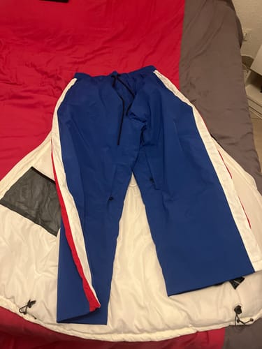Customer's blue baggy snow pants with red and white side stripes laid out flat on a bed.