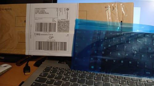 Un client montre le nouveau clavier Lenovo sous son film protecteur bleu, posé sur le portable à côté de sa boîte d'expédition.