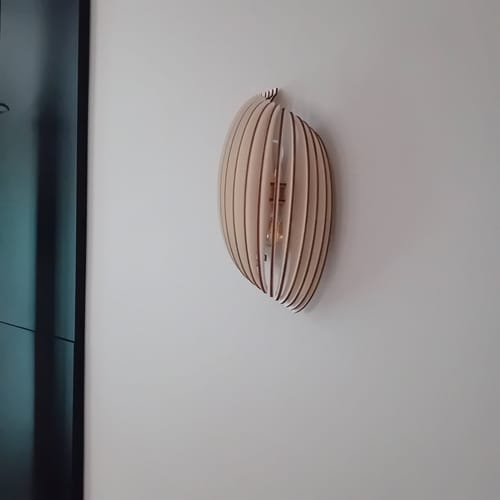 Avis d'un client : l'applique murale Assia en bois clair, allumée et installée sur un mur blanc.