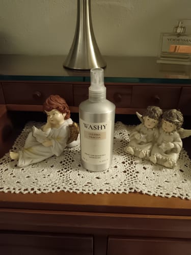 Recensore mostra lo spray antiodore L'Ultima Traccia su un comò in legno, accanto a delle statuine decorative.
