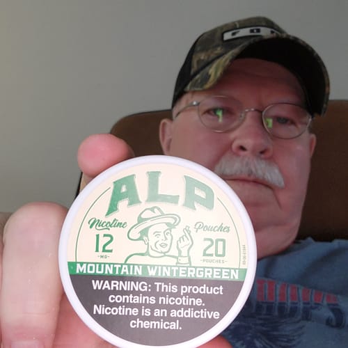 Reviewer holding up a white can of ALP Mountain Wintergreen Nicotine Pouches.
