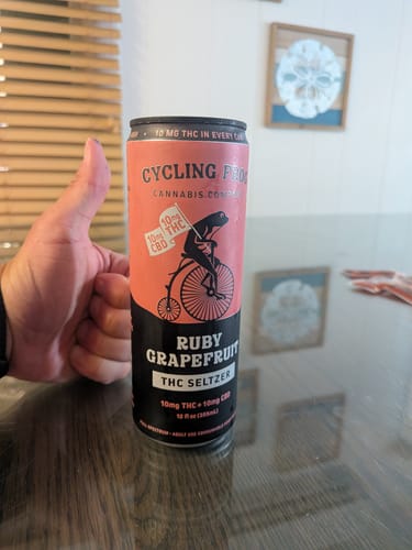Reviewer giving a thumbs-up to a can of THC seltzer sitting on a glossy table.