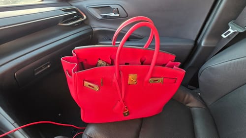 Customer's bright red LALUVA Warkin Bag with gold hardware resting on a car passenger seat.
