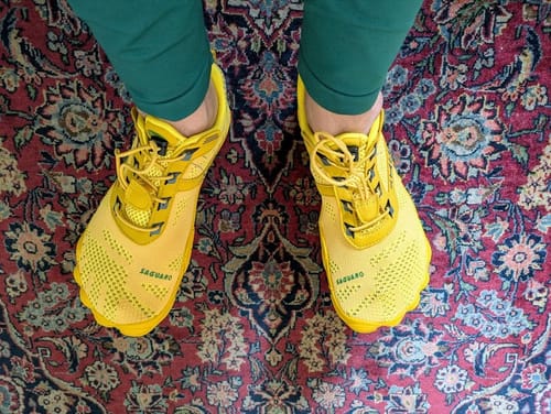 A reviewer's top-down view of their bright yellow Free Ⅰ - Barefoot Shoes while standing on an ornate rug.