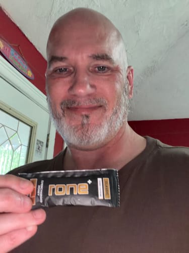Reviewer smiling while holding up a single packet of Classic SuperCharged Honey.