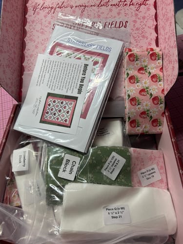 Reviewer's open Strawberry Fields Quilt Kit box, showing colorful precut fabrics and the instruction booklet.