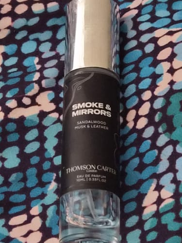 Customer's Smoke & Mirrors perfume bottle with a sleek black label and silver cap, shown against a patterned background.