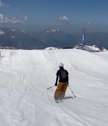 Customer skiing down a snowy slope toward a jump while wearing the baggy snow pants.