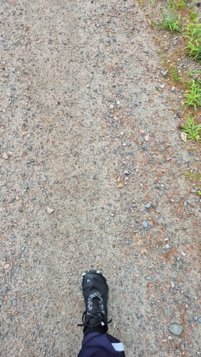 Asiakkaan musta Vaistoa Lento -paljasjalkajuoksukenkä jalassa soratiellä.