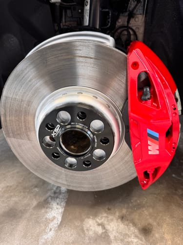 Close-up of a reviewer's black wheel spacer installed on a BMW hub next to the bright red brake caliper.