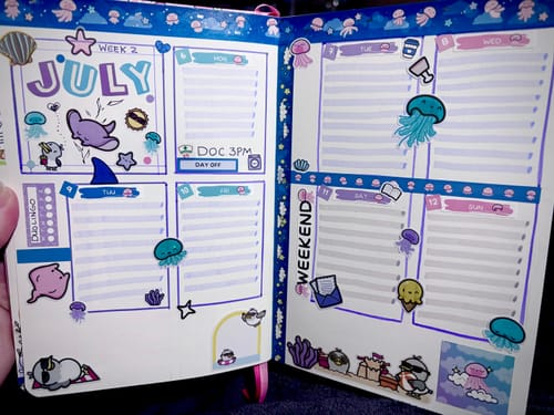 Reviewer's hand holding a planner open to a July spread decorated with cute jellyfish stickers from the Dreamy Jellies set.