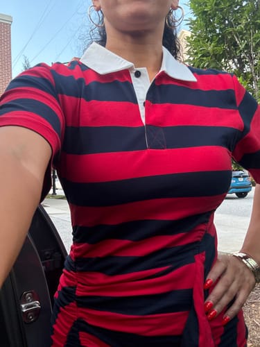 Customer wearing a red and navy striped polo dress with a white collar and side ruching.