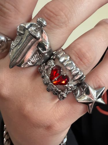 Customer's hand wearing the shiny MINI PROMISE RING with a red heart stone, styled between other silver rings.
