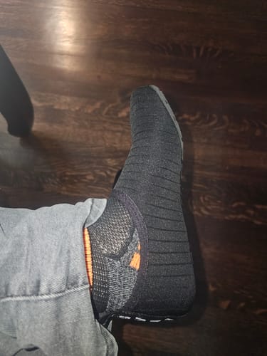 Customer wearing a black, textured Touch IV shoe, showing the top of the foot and orange inner accent.