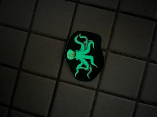 Customer's glow-in-the-dark octopus sticker glowing green on a dark tiled surface.
