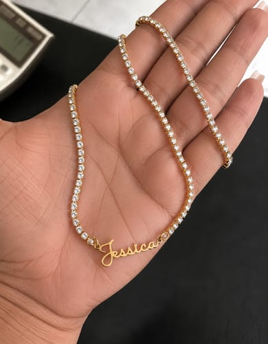 Reviewer's hand holding a sparkling, gold Signature Name Tennis Necklace with the name 'Jessica' in a script font.