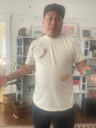 Reviewer wearing the off-white Hotdog Dive — Premium Tee with cartoon hotdog graphics indoors.