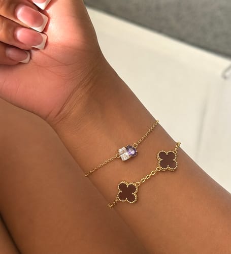 Reviewer's wrist wearing the gold Forever Duo Birthstone Bracelet with purple and clear stones, layered with another bracelet.
