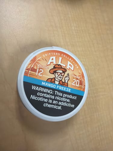 Customer's round tin of Drifters Mango Freeze Nicotine Pouches on a wooden surface.