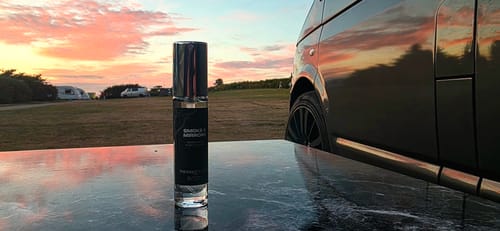 Customer's Smoke & Mirrors perfume bottle on a reflective surface outdoors at sunset.