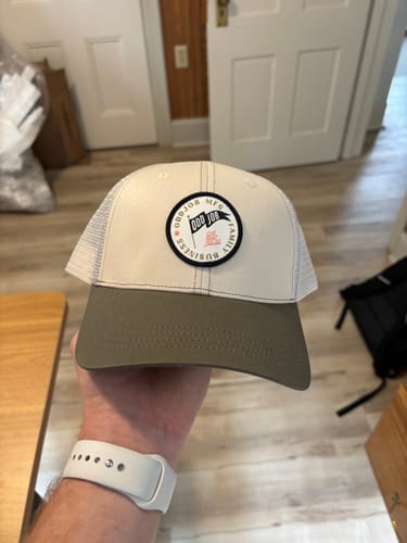 Customer holding a beige and olive green Big Trucker Hat with a circular front patch and mesh back.