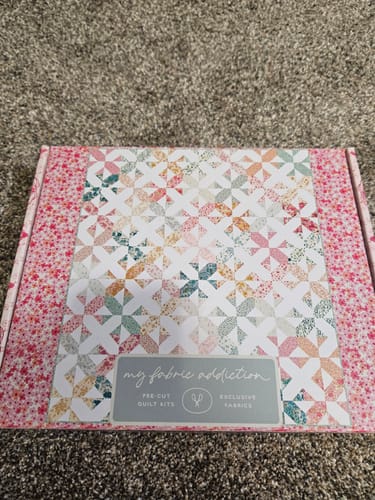 Customer shows the box for their Bloomcross Precut Quilt Kit, with the colorful finished quilt design on the lid.