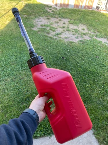Customer holding the red 1.25 Gallon Jug by its handle outdoors, with the auto-stop spout attached.