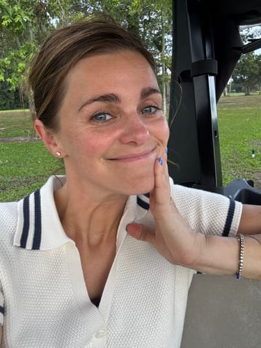 Reviewer smiling, showing the Luxe Tennis Bracelet on their wrist while seated in a golf cart.