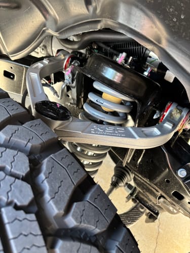 Customer's silver Forged Aluminum Upper Control Arm installed in the wheel well next to the tire and suspension.