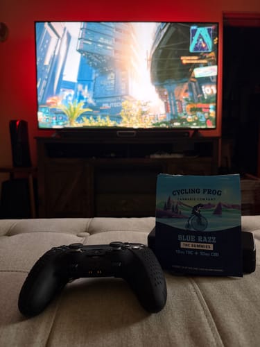 Reviewer's Blue Razz Gummies next to a game controller, with a video game on a TV in the background.