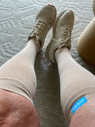 A reviewer shows their legs in beige ribbed support socks with a small blue tag, paired with sneakers.