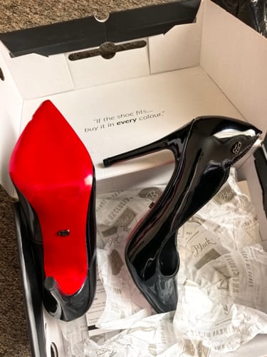 Customer's shiny black Miss Black Lola 1 Court heels in the shoebox, with one showing its vibrant red sole.