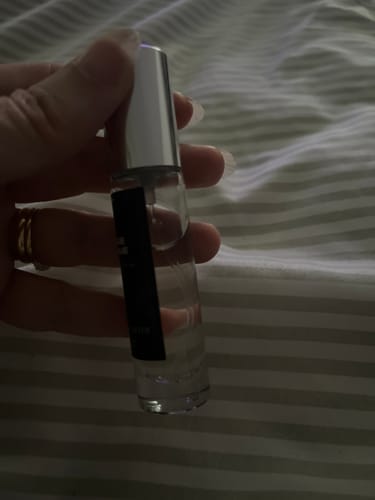 Close-up of a customer holding a small bottle of Lilium Blume Eau de Parfum against a striped surface.