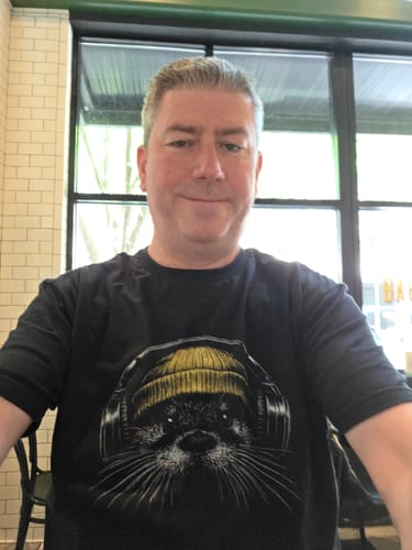 A reviewer wearing the black Otter Tune t-shirt with its graphic of an otter in a beanie and headphones.