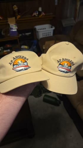 Reviewer holding two tan hats with the "AP ANGLERS" custom embroidery.