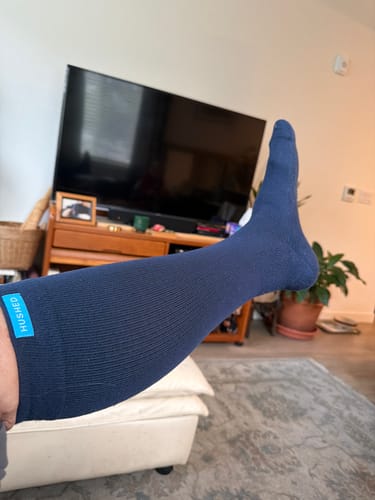 Customer's leg propped up, wearing a navy Eucalyptus Lyocell Compression Sock, showing the fit up to the calf.