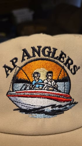 Close-up: Customer's tan hat with custom embroidery of two people in a boat under the text "AP ANGLERS."