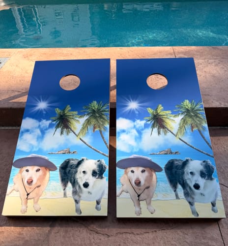 Customer's two cornhole boards with Custom Cornhole Board Wraps featuring a tropical beach scene with two dogs.