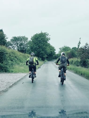 Two customers seen from behind, wearing Cryptkeeper All Season Trail Shorts while cycling on a wet road.